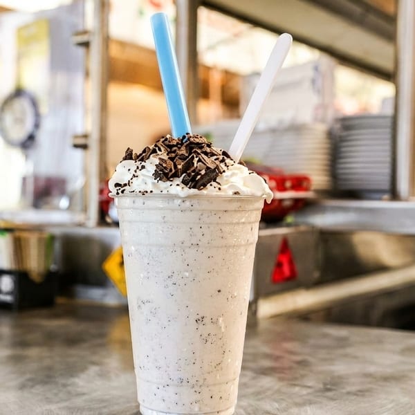 Cookies and cream milkshake with whipped cream, chocolate shavings, and two straws on a counter.