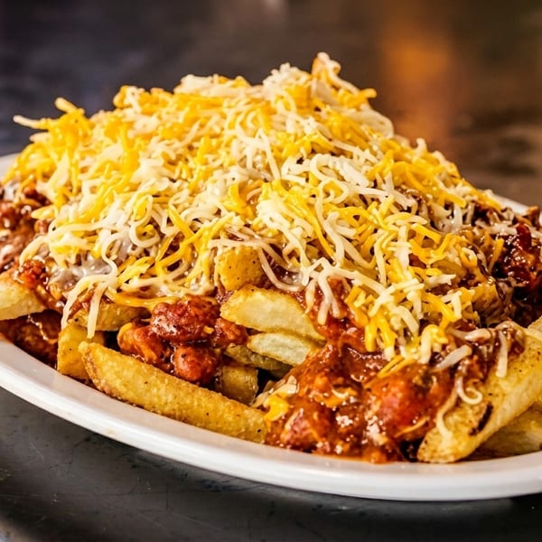A white plate piled high with golden french fries, smothered in chili and shredded cheese.
